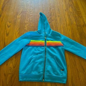 A zip up hoodie with turquoise and 5 different colored stripes